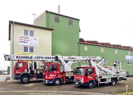 Gebäude, davor drei parkende rote Arbeitsbühnen.