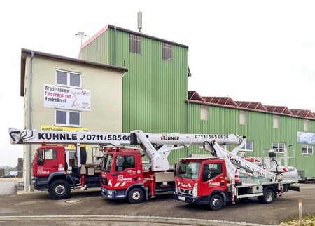 Gebäude, davor drei parkende rote Arbeitsbühnen.
