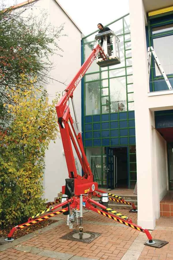 Rote ausgefahrene Arbeitsbühne mit Person vor Fensterfront eines Gebäudes.