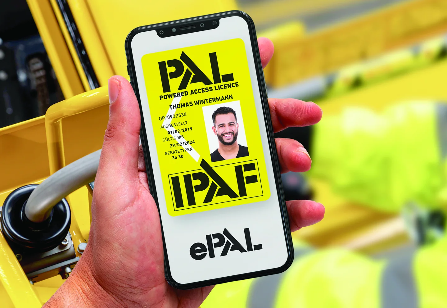 Person in Schutzkleidung auf Arbeitsbühne, hält ein Handy in der Hand.