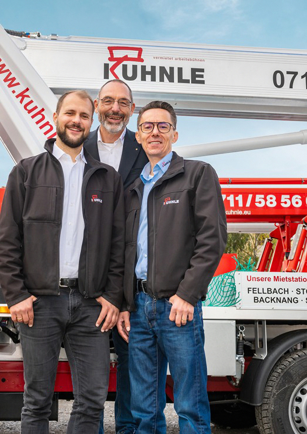 Drei Männer in Arbeitskleidung vor Arbeitsbühne
